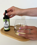 Hand holding a bottle labeled 'Bio Chaga' above a glass of liquid on a wooden tray.